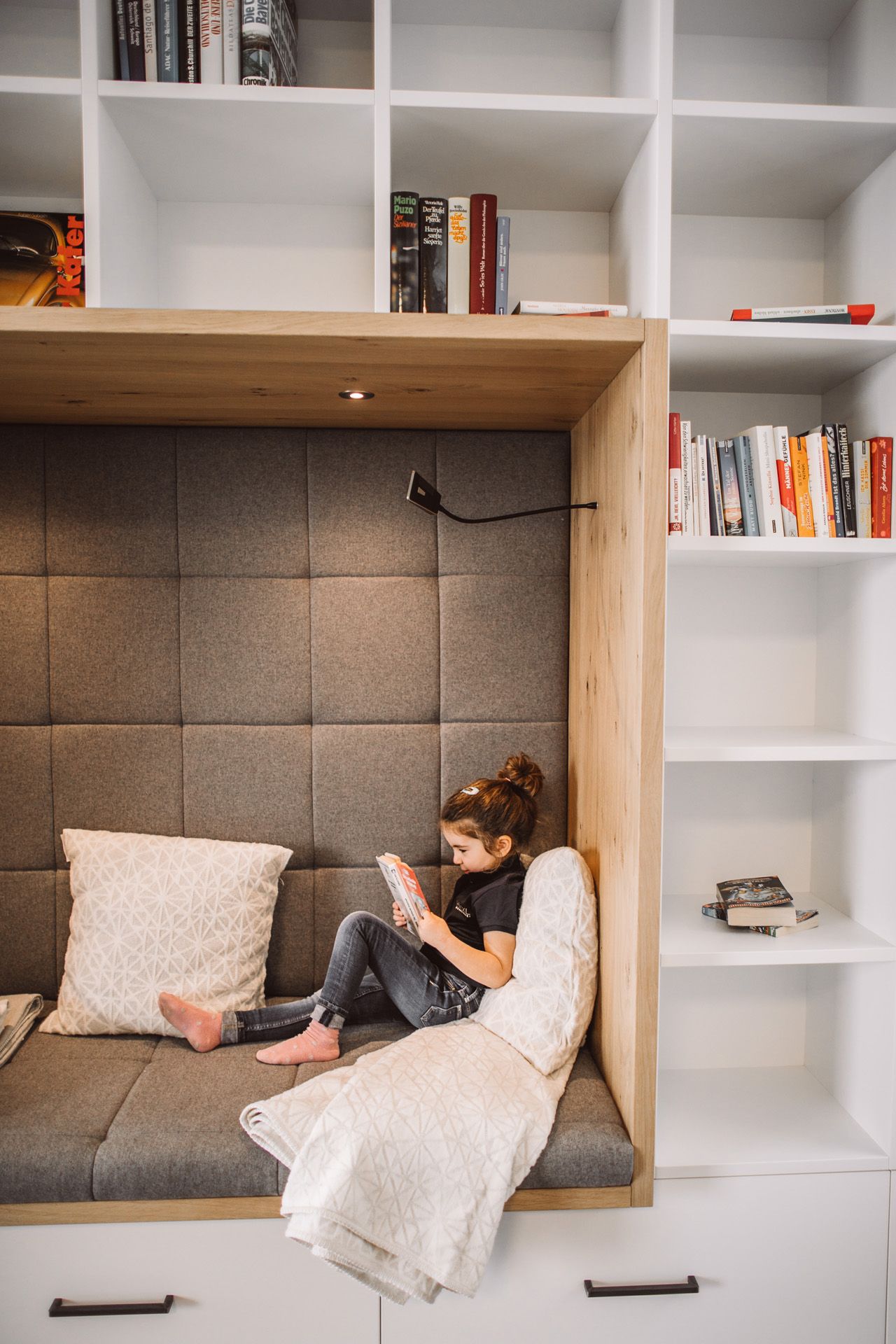 Kleines Mädchen liest in einer kuscheligen Nische, eingelassen in das Bücherregal