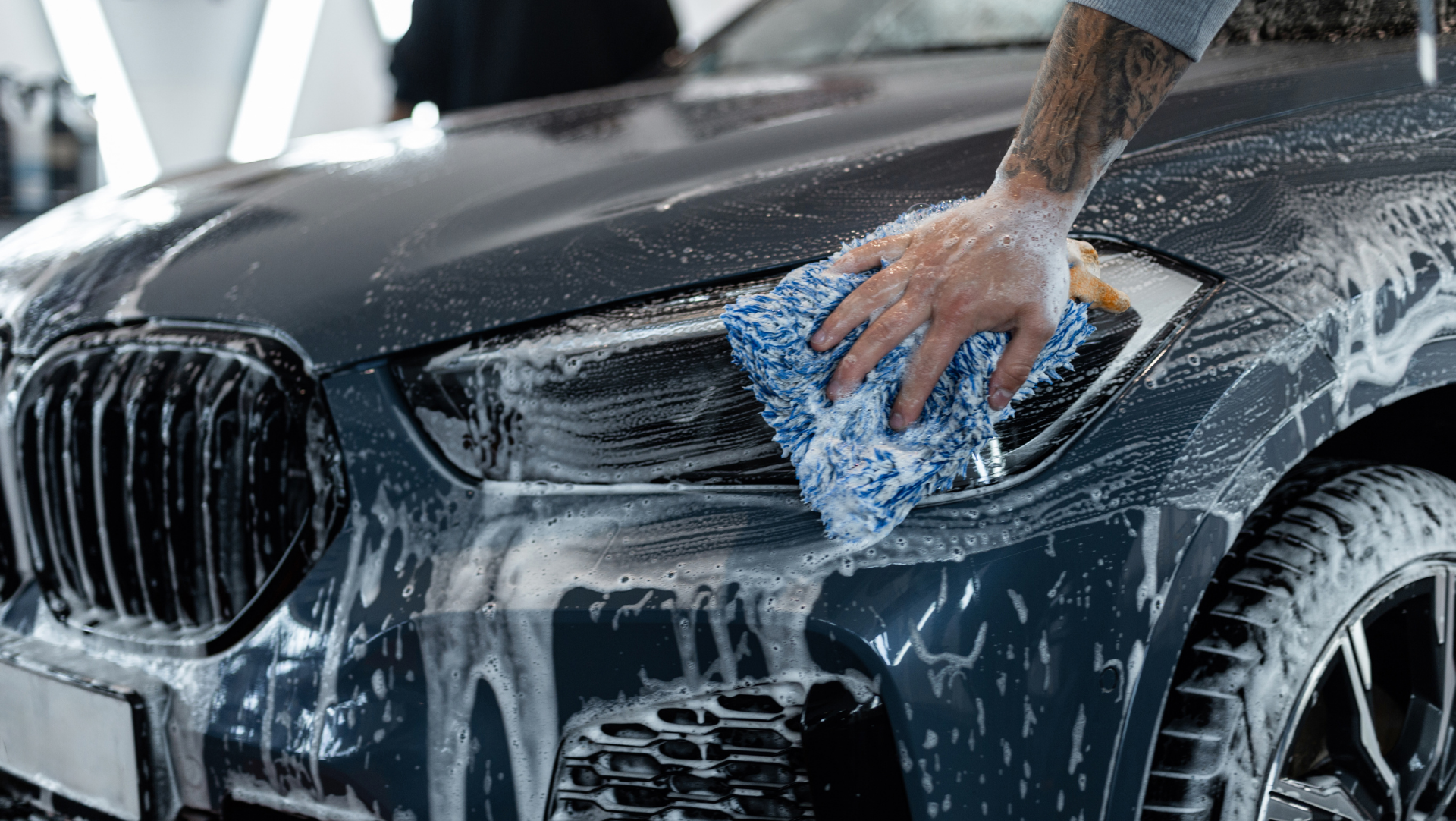 Un homme lave une voiture avec une éponge et du savon.