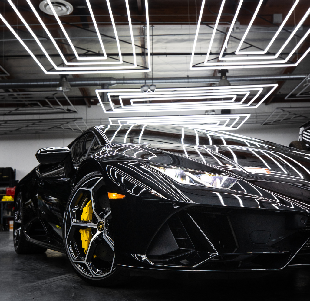 Une voiture de sport noire est garée dans un garage sous des néons