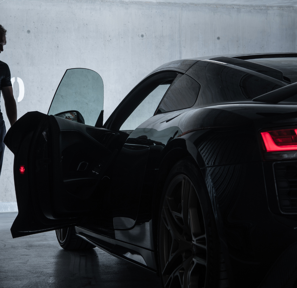 Un homme debout à côté d'une voiture de sport noire avec la porte ouverte