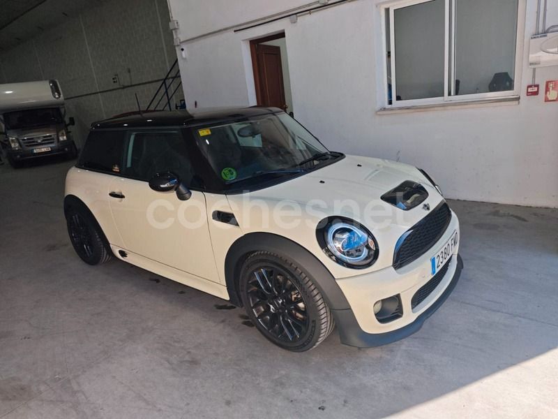 Un Mini Cooper de color crema con techo y ruedas negras estacionado dentro de un almacén.