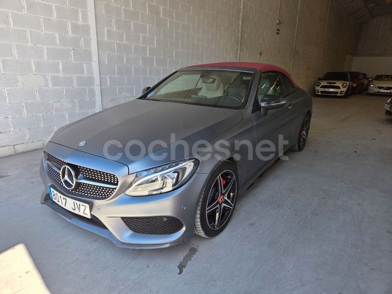 Un Mercedes-Benz descapotable gris estacionado en un almacén con poca luz y paredes de bloques de hormigón.