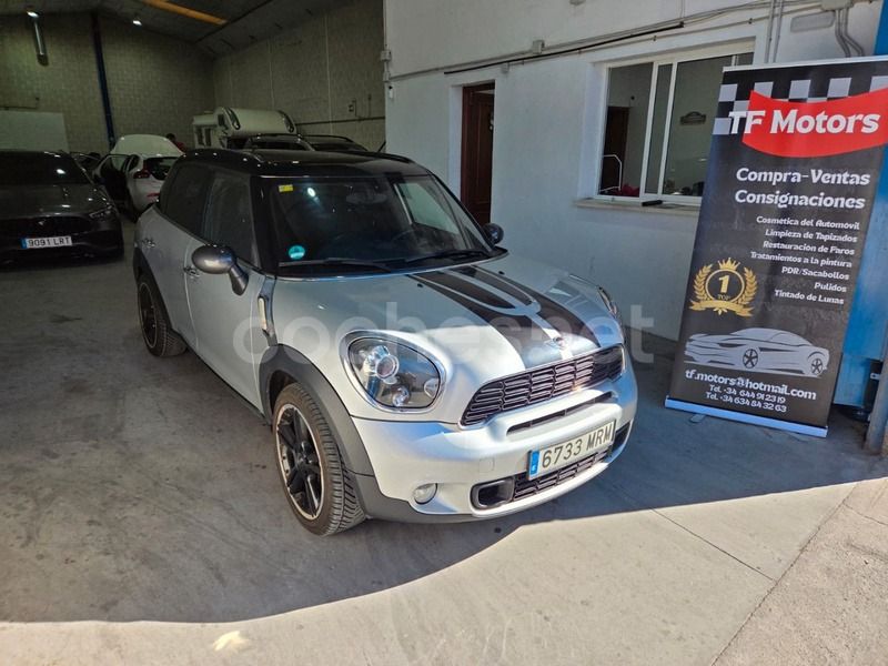 Un Mini Countryman plateado con techo negro aparcado dentro de un garaje junto a un cartel de la marca TF Motors.