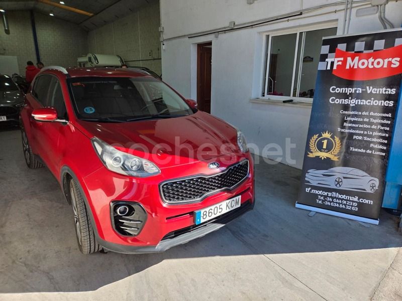 Un SUV Kia rojo estacionado en un garaje junto a un cartel publicitario de TF Motors.