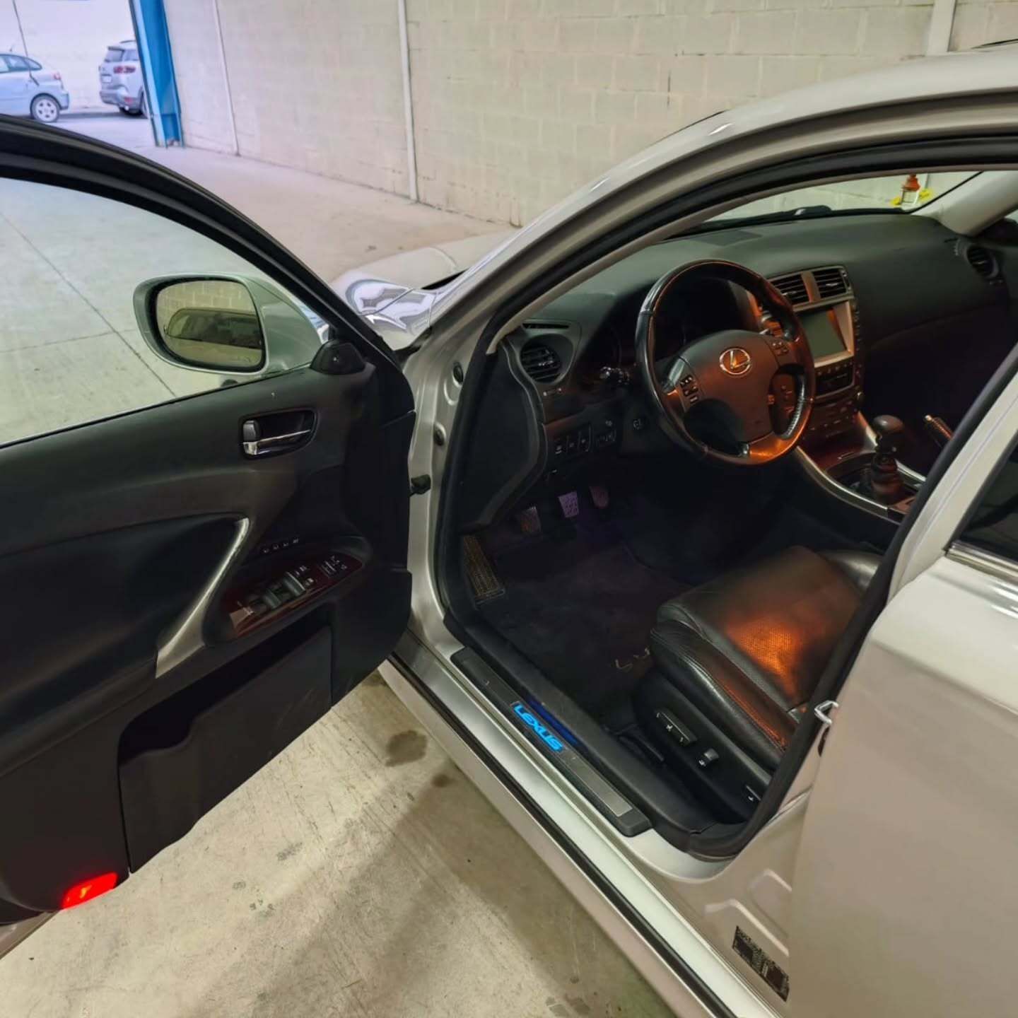 Al abrir la puerta del lado del conductor de un sedán Lexus plateado, se puede apreciar un interior de cuero.