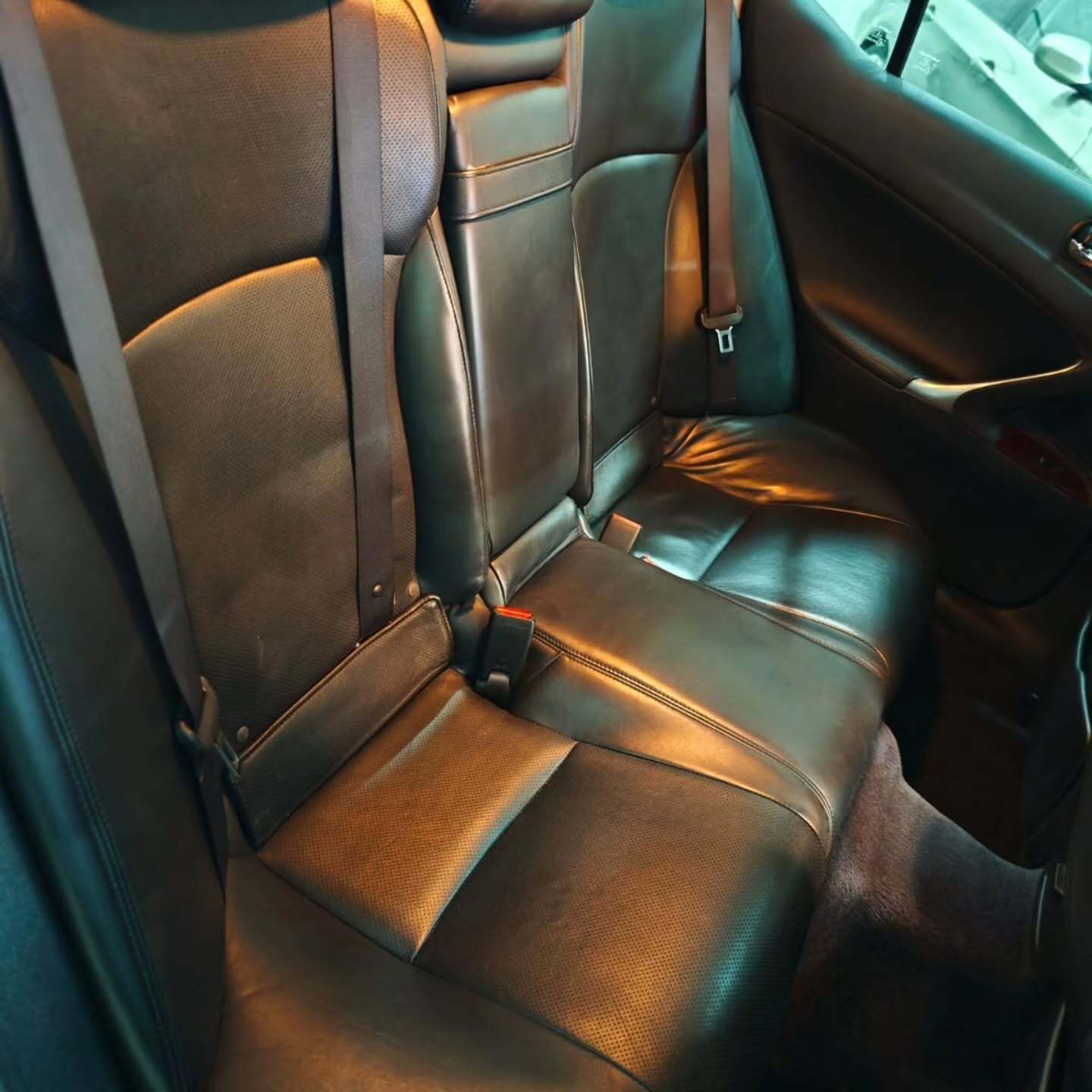 Primer plano de la tapicería de cuero oscuro del asiento trasero del coche, incluyendo los cinturones de seguridad.