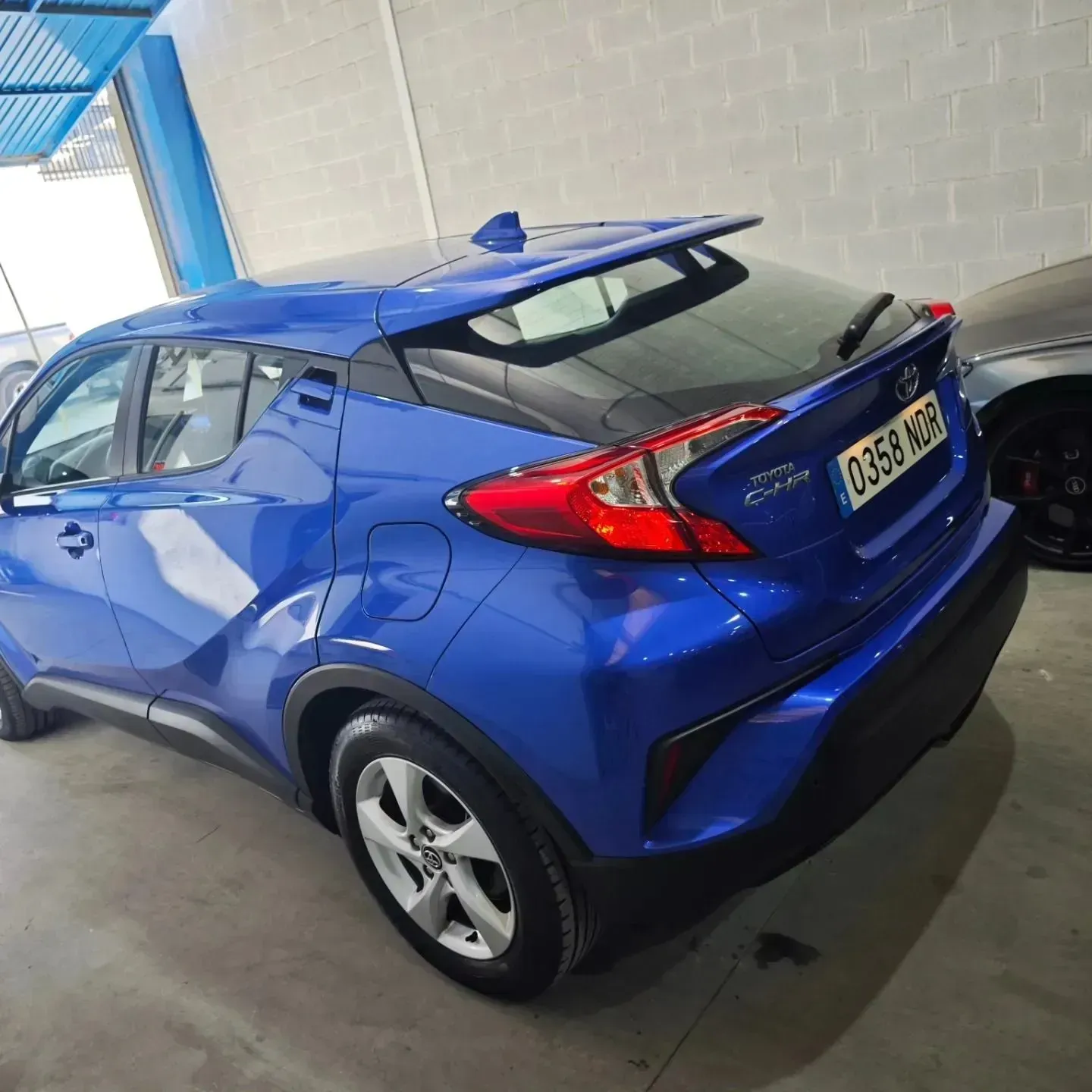 Un Toyota C-HR azul estacionado en el interior de un garaje, visto desde un ángulo de tres cuartos trasero.