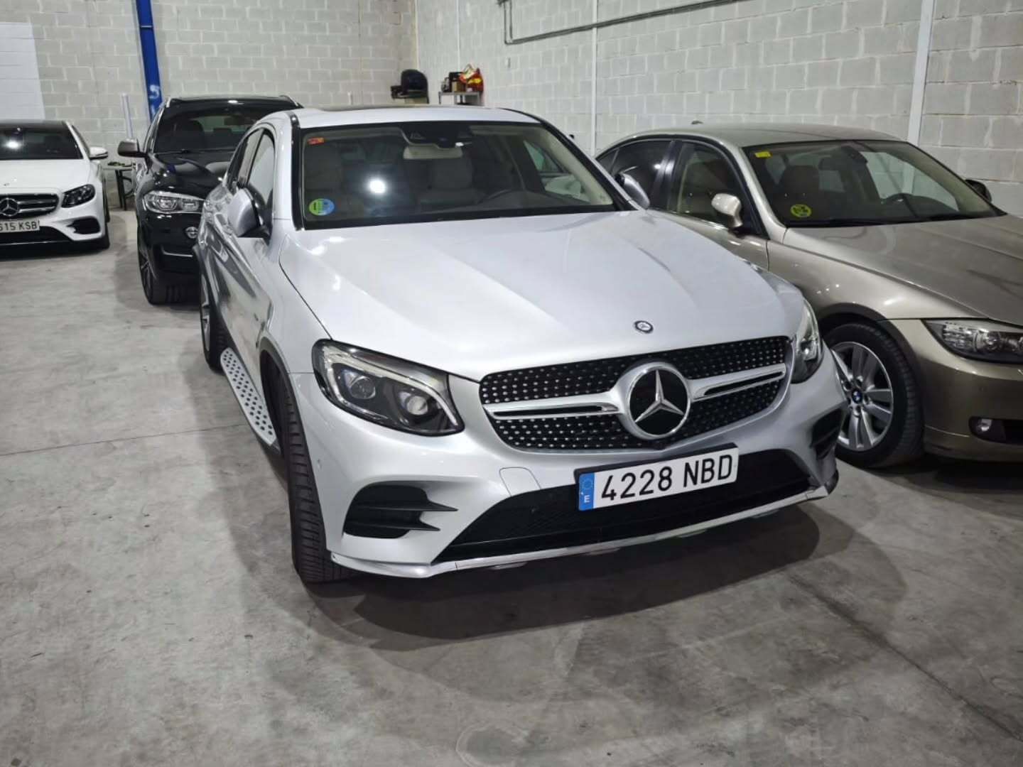Un SUV Mercedes-Benz plateado estacionado en un garaje cubierto, flanqueado por otros vehículos.