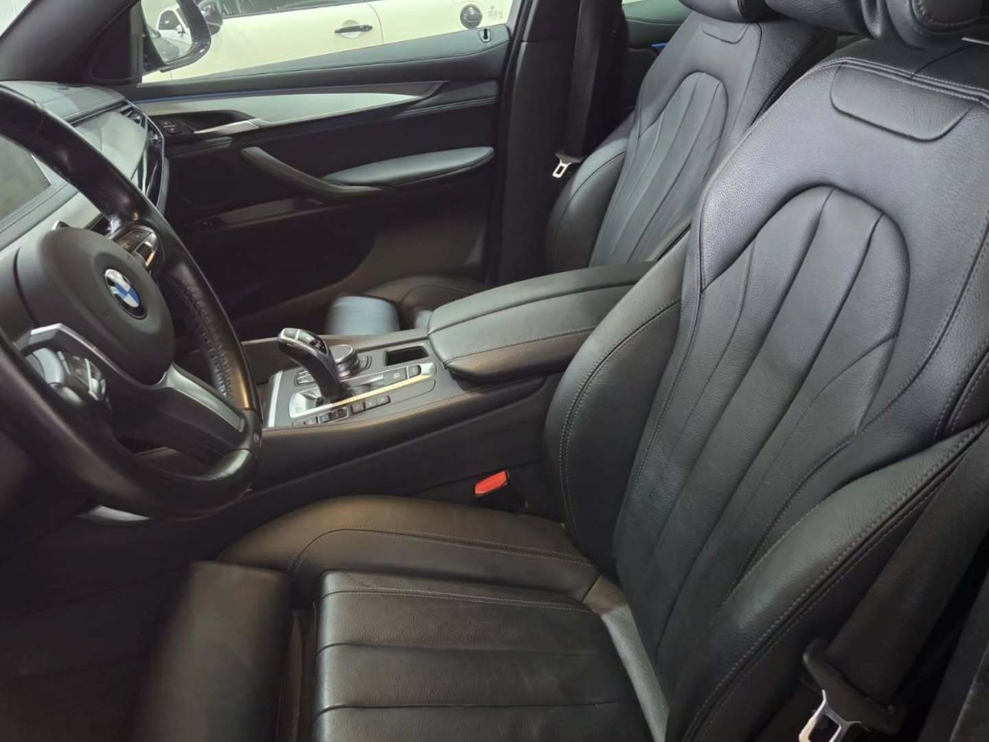 El interior de un coche BMW, con asientos de cuero negro, un volante con el logotipo de BMW y una consola central.