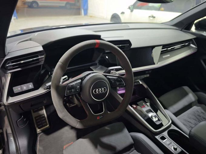 El interior de un Audi moderno, con un volante de Alcantara oscuro con una franja roja en el centro.