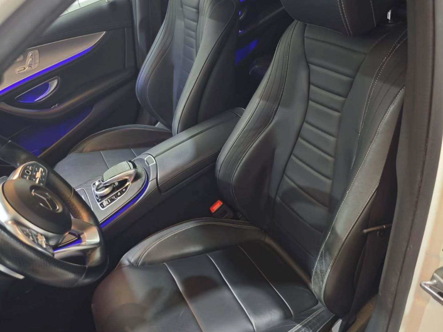 Interior del coche en cuero negro con asientos deportivos con costuras blancas e iluminación ambiental azul.