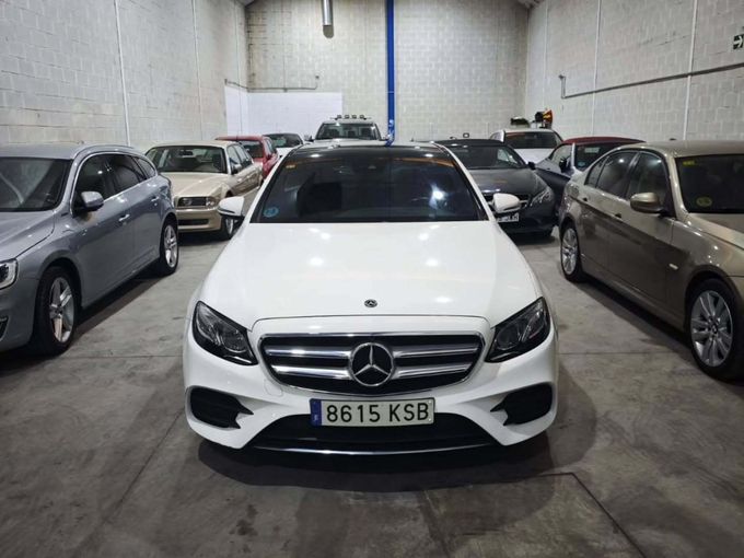 Un Mercedes-Benz blanco estacionado en el garaje de un almacén, rodeado de otros coches.
