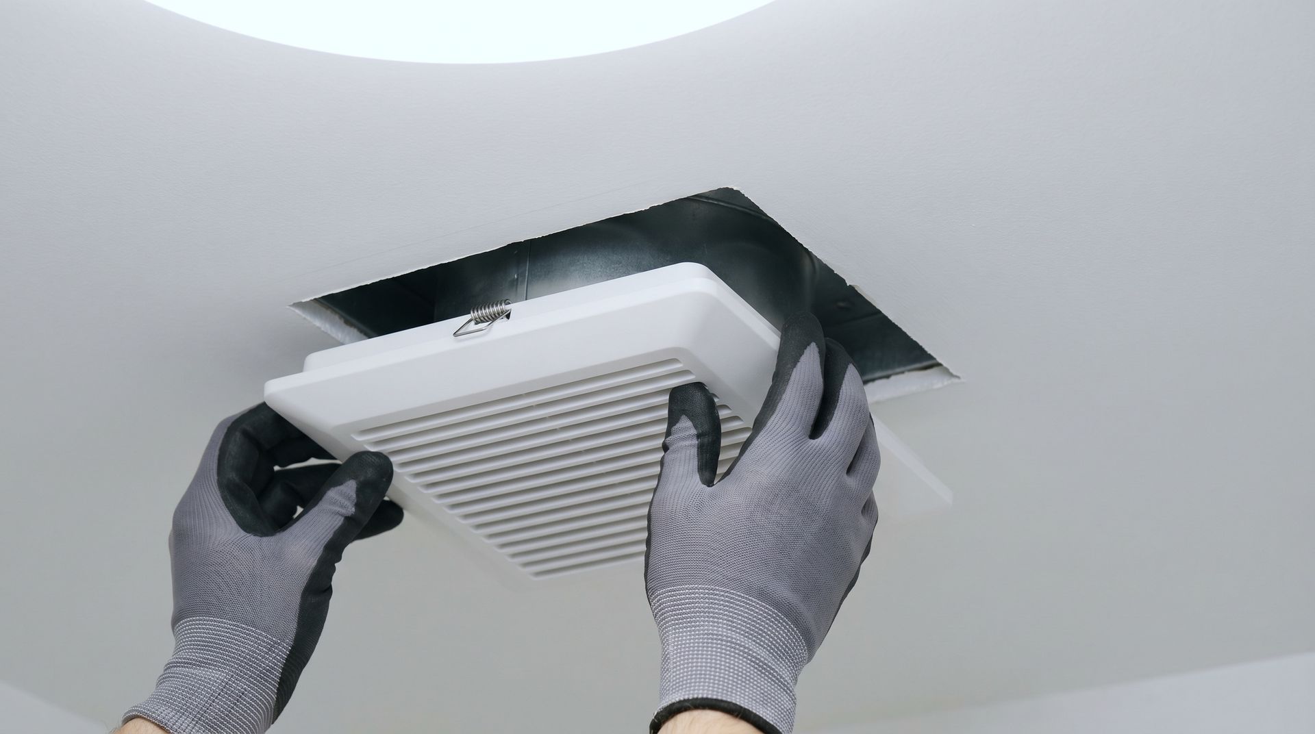 Des mains gantées installent une grille d'aération dans un plafond blanc.