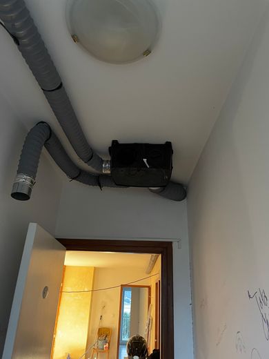 Plafond du couloir avec conduits apparents et grille d'aération noire au-dessus d'une porte.