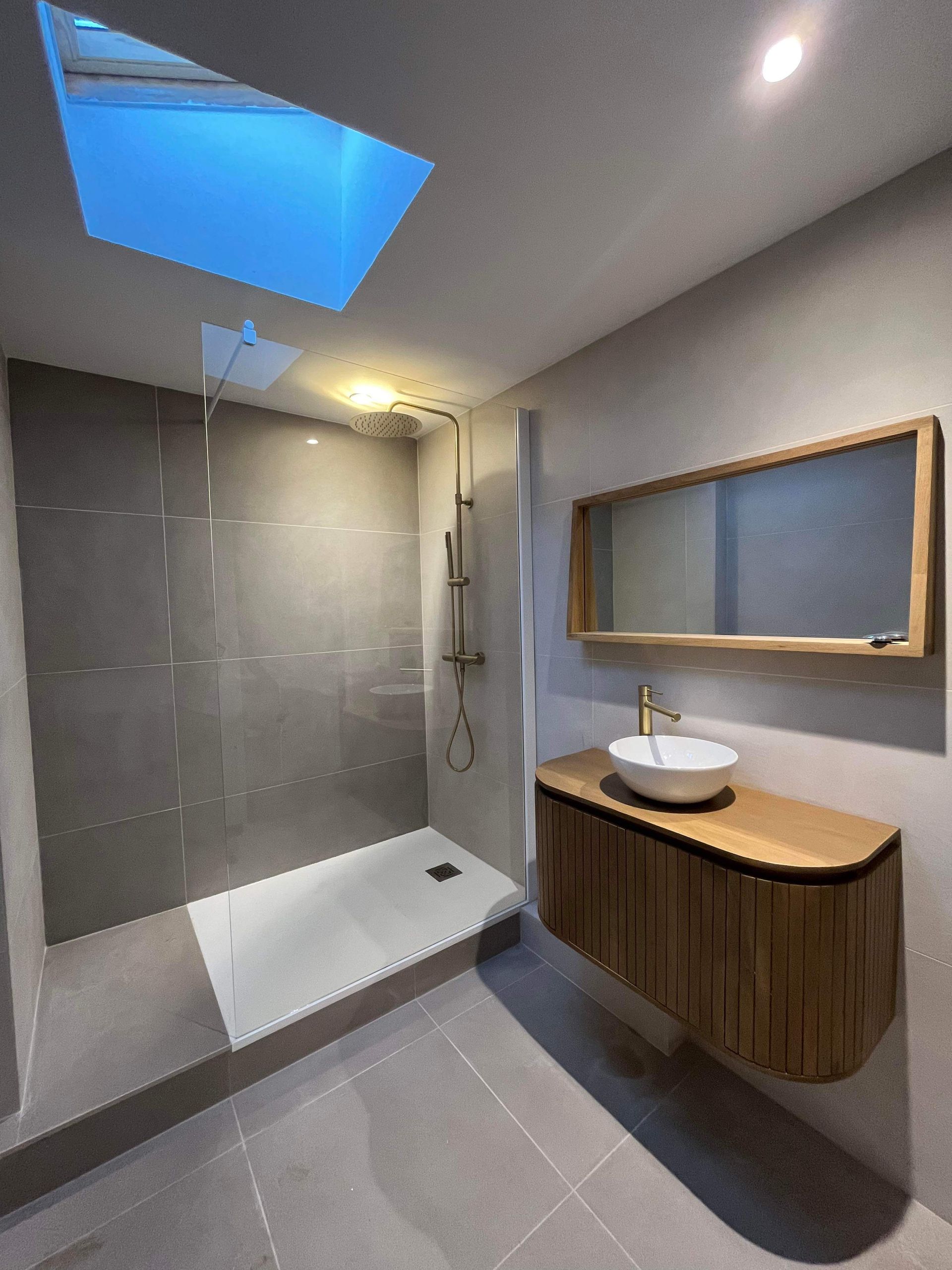 Salle de bains moderne grise avec douche à l'italienne, puits de lumière et meuble lavabo en bois avec vasque ronde.