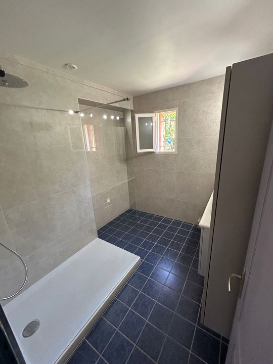 Salle de bains avec baignoire blanche, sol carrelé bleu foncé, murs beiges et petite fenêtre.