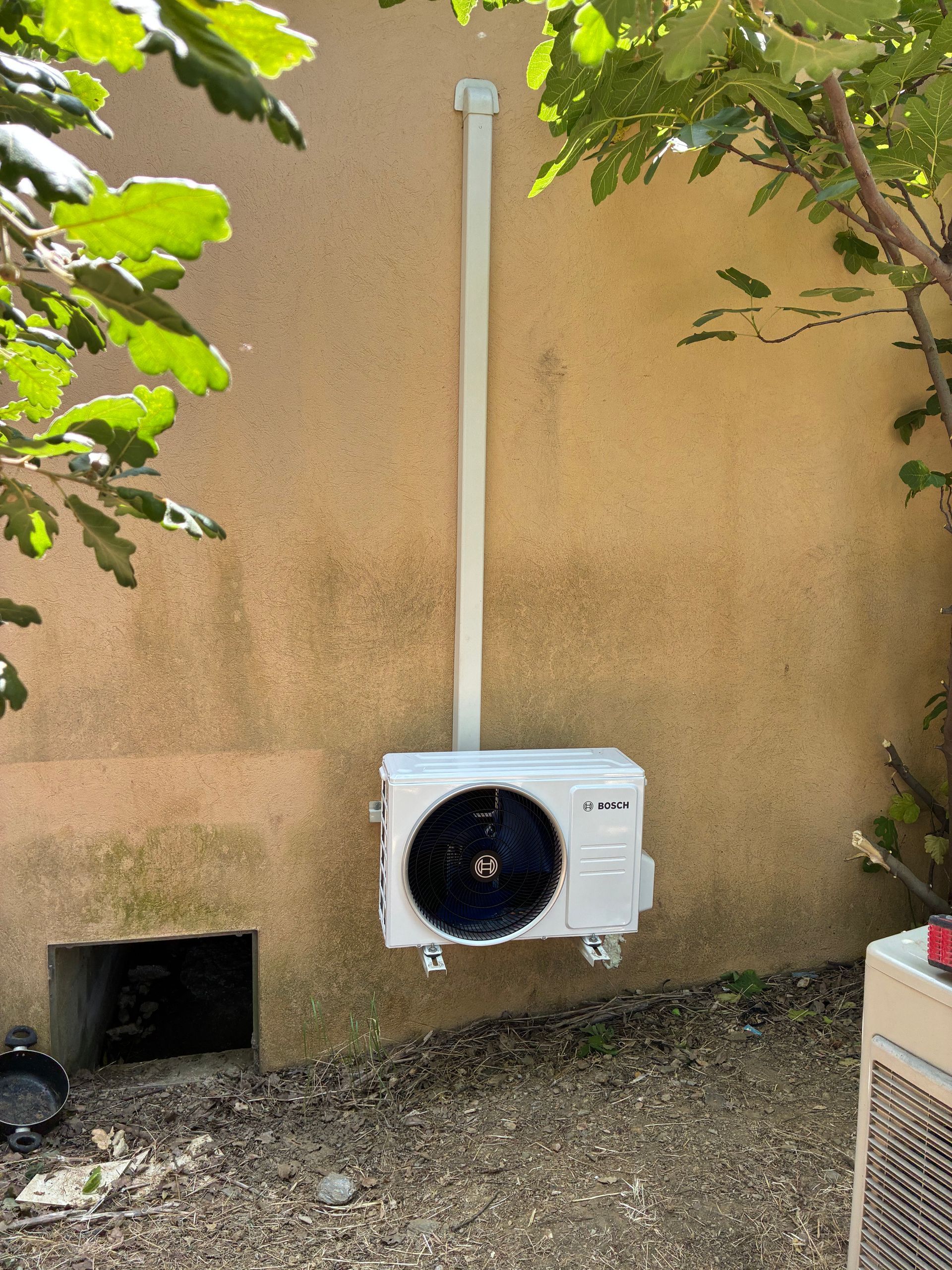 Unité de climatisation extérieure fixée sur un mur beige.