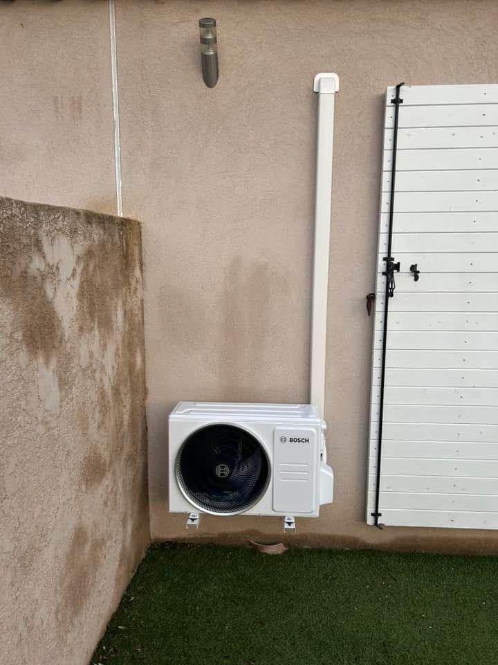 Balcon extérieur avec un climatiseur blanc à côté d'une porte coulissante en verre et d'une rambarde.