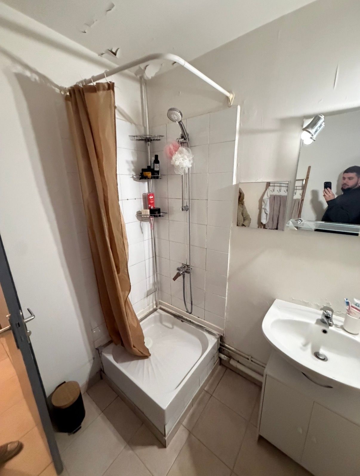 Salle de bain compacte avec douche, rideau marron, lavabo et miroir mural montrant une personne prenant la photo