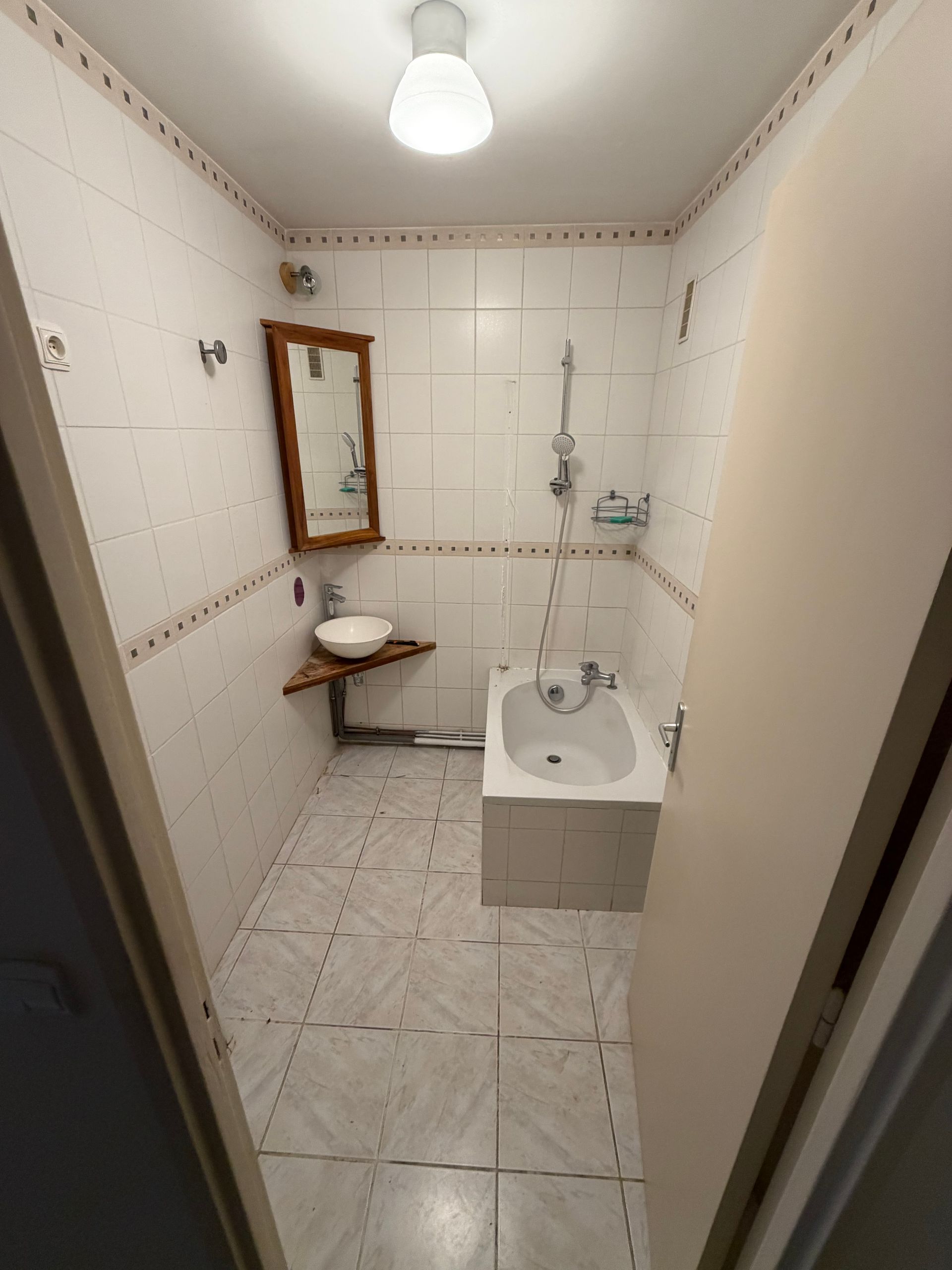 Petite salle de bains carrelée avec lavabo, miroir, douche et toilettes sous un plafonnier.