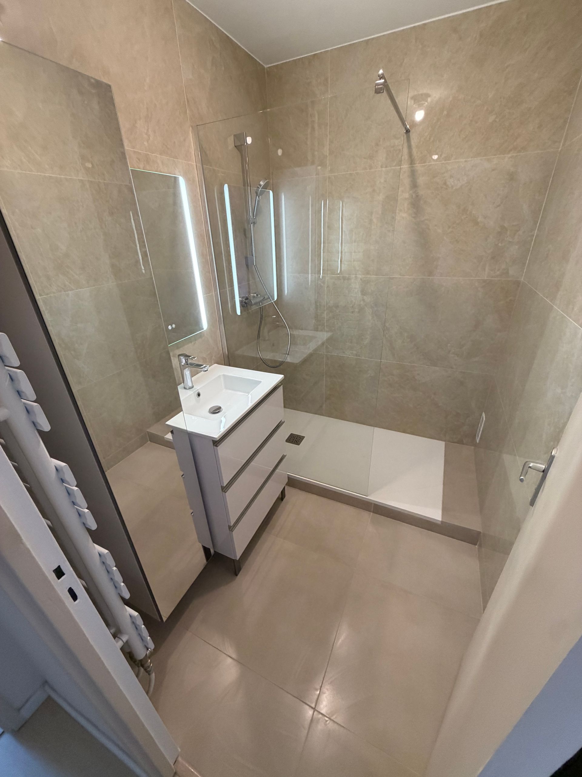 Salle de bains moderne beige avec douche à l'italienne, lavabo, grand miroir et cloison en verre