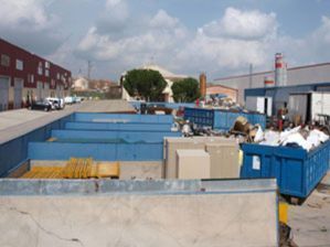 Un contenedor de basura azul está lleno de basura frente a un edificio.