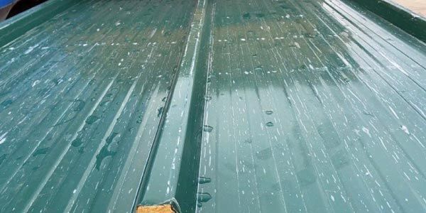 Un primer plano de un techo de metal verde con gotas de agua sobre él.