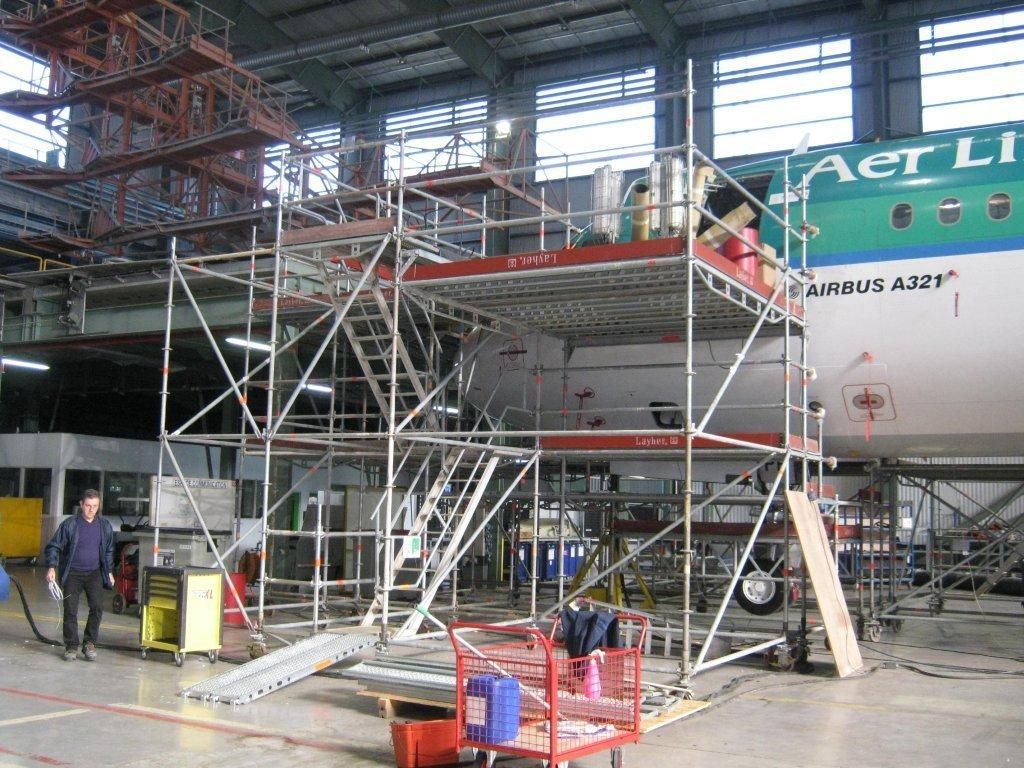 Échafaudage à côté d'un avion dans un hangar, avec un ouvrier à proximité