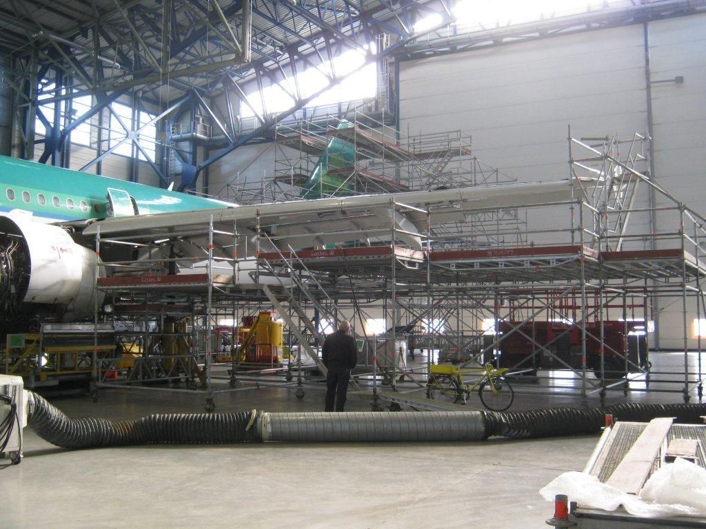 Un avion se trouve dans un hangar, entouré d'échafaudages pour maintenance