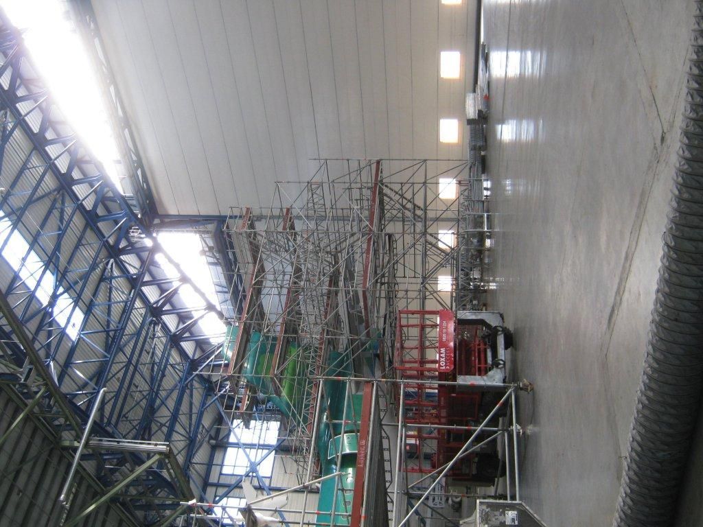 Dans un grand hangar, des échafaudages et du matériel entourent un objet en réparation