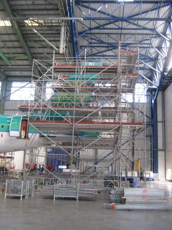 Des échafaudages entourent le fuselage d'un avion à l'intérieur d'un hangar