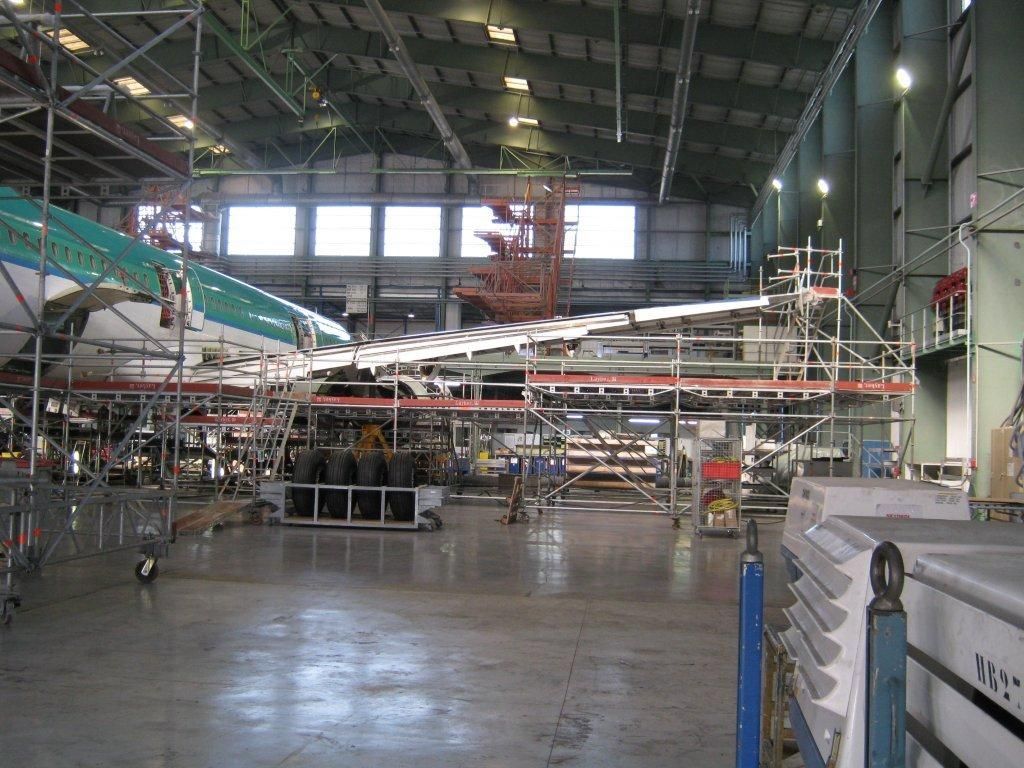 Une aile d'avion est en cours de maintenance dans un grand hangar, entourée d'échafaudages et d'outils.