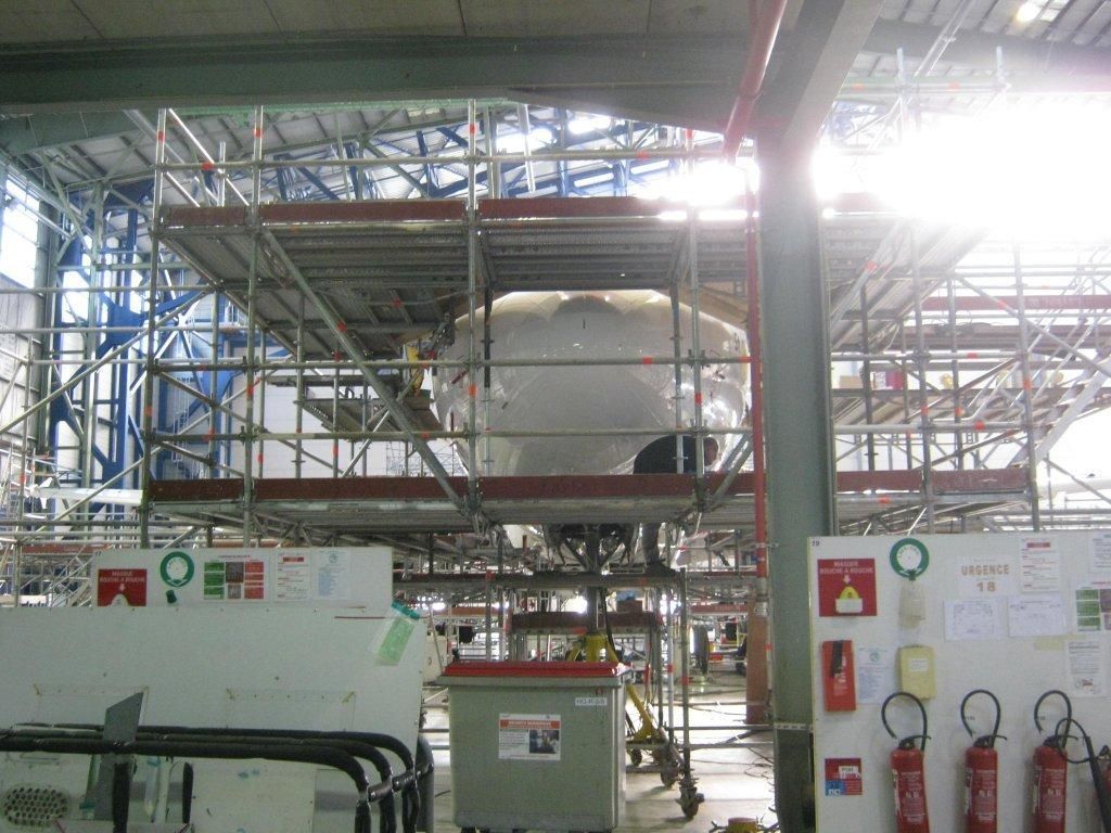 Composant d'avion blanc entouré d'échafaudages à l'intérieur d'un grand bâtiment industriel
