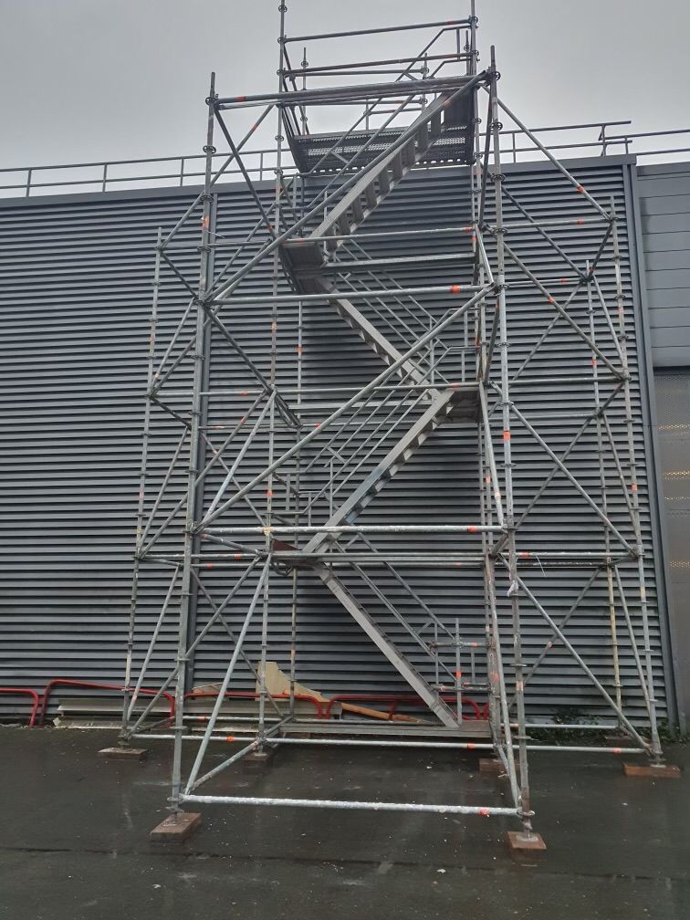 Échafaudage avec escalier contre un bâtiment au bardage argenté
