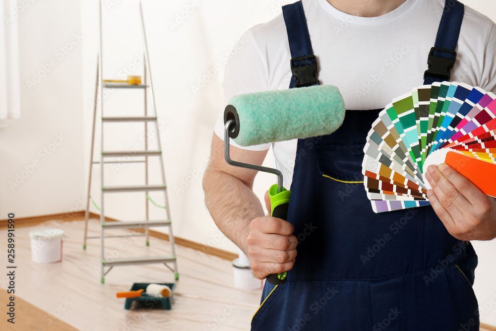Une personne tenant un rouleau à peinture et des échantillons de couleur dans une pièce en cours de peinture