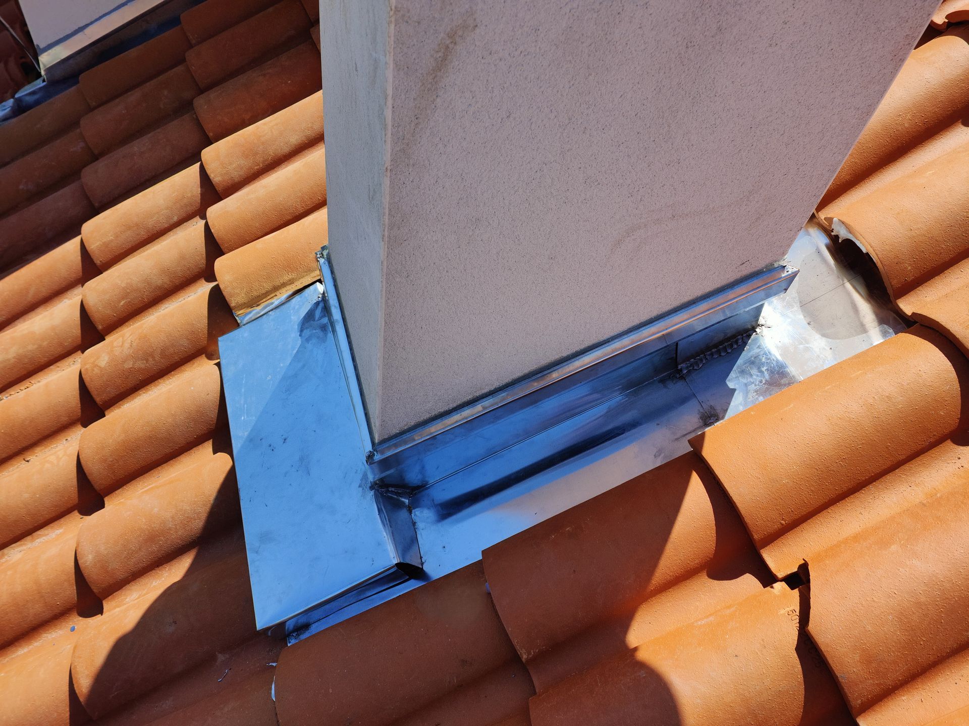 Solin de cheminée sur toiture en tuiles orange, avec mastic bleu à la base