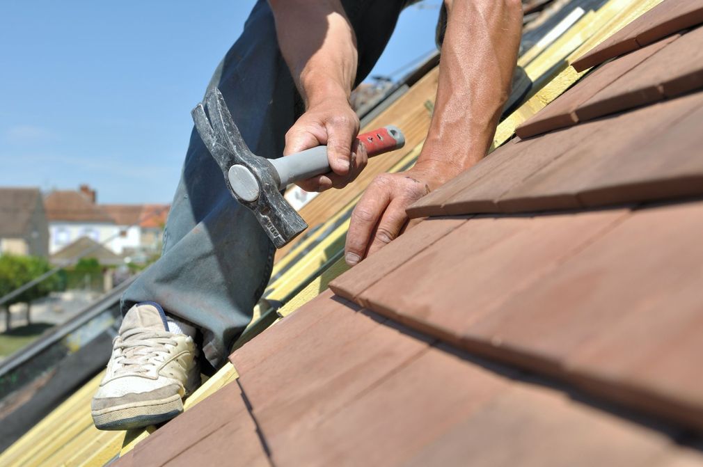 Un couvreur cloue des bardeaux sur un toit en pente en construction