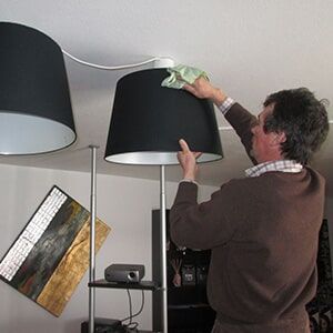 Pessoa limpando um abajur preto com um pano, em ambiente interno.