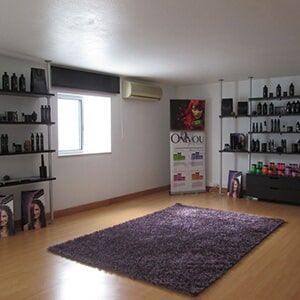 Interior de um salão de cabeleireiro com prateleiras de produtos, um tapete felpudo e cartazes promocionais.