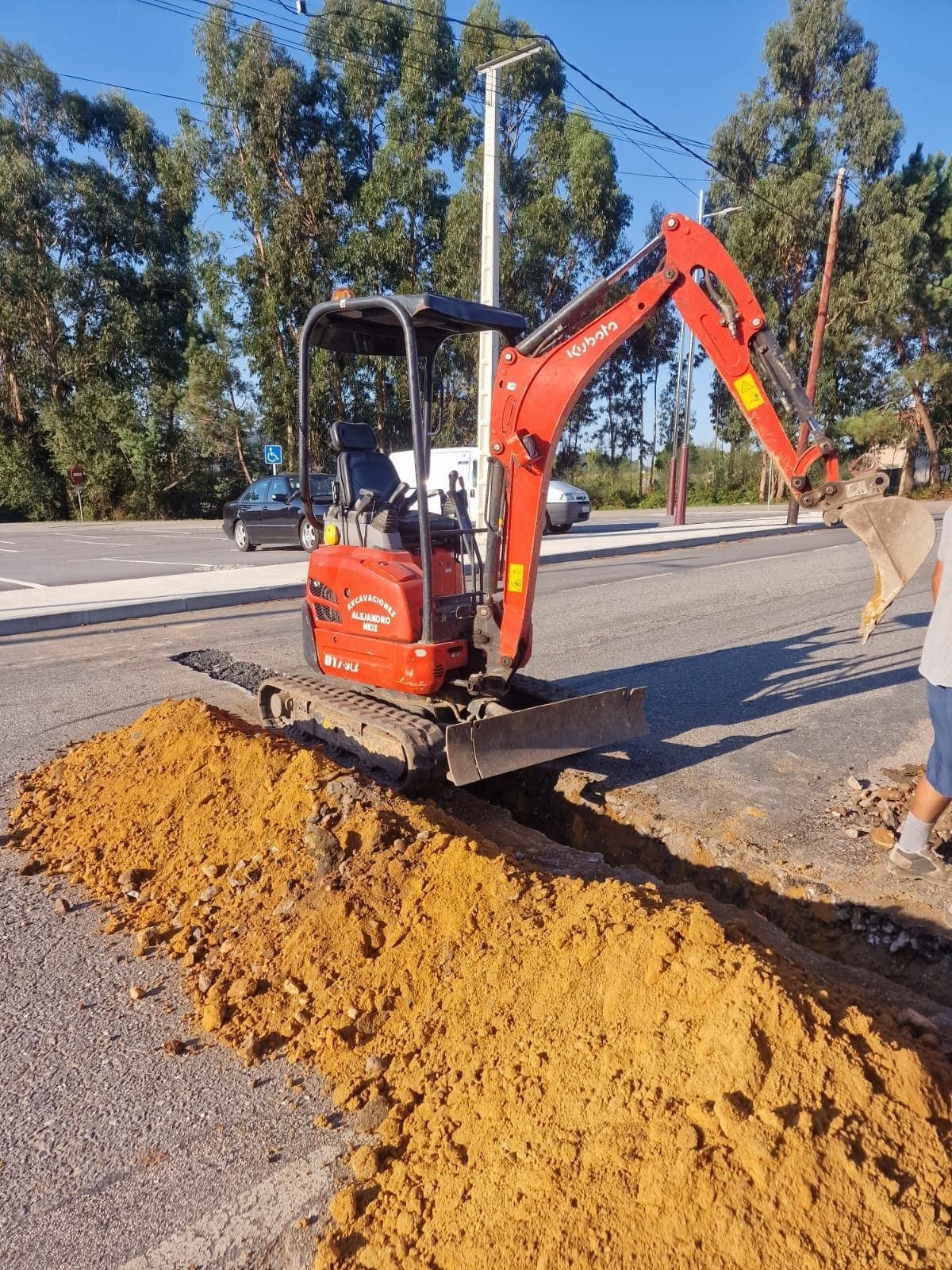 Miniexcavadora extendiendo un montón de tierra en una obra de construcción al borde de la carretera.