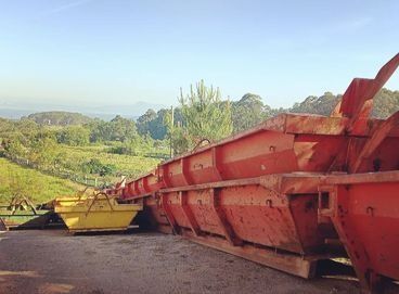 Cinta transportadora de construcción roja y amarilla en un paisaje rural bajo un cielo azul.