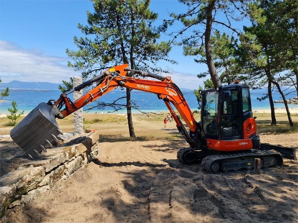 Excavadora naranja cargando tierra junto a una playa con árboles y agua azul al fondo.