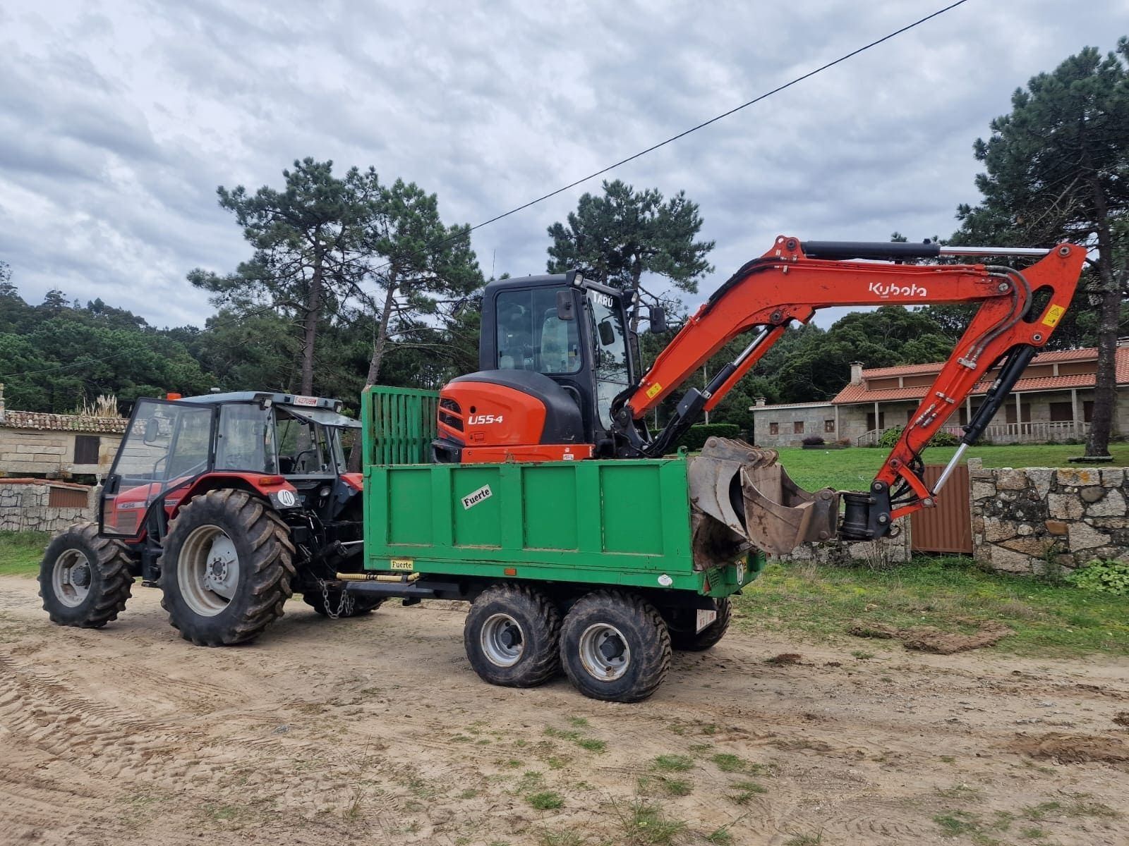 Excavadora naranja montada sobre un remolque verde enganchado a un tractor en un campo rural.