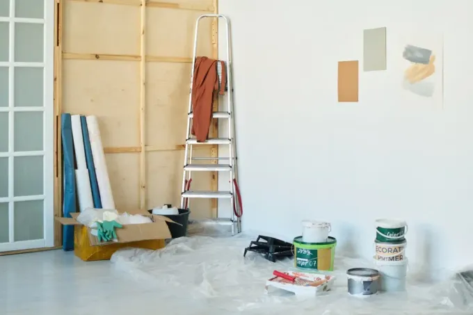 Renovación de habitación interior en progreso: escalera, latas de pintura, muestras de pintura y materiales.