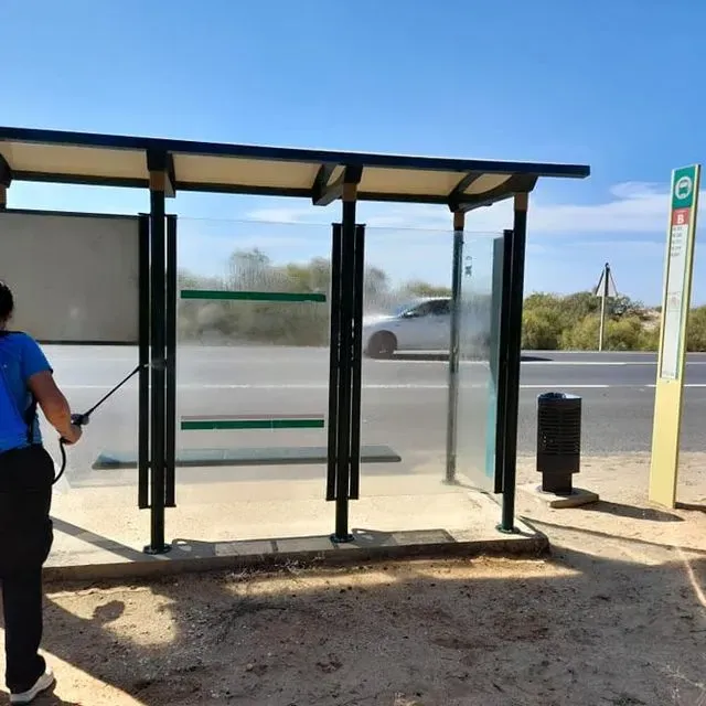 Una persona rociando una parada de autobús con una manguera