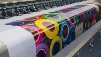 Una impresora grande está imprimiendo una hoja grande de papel con un diseño colorido en ella.