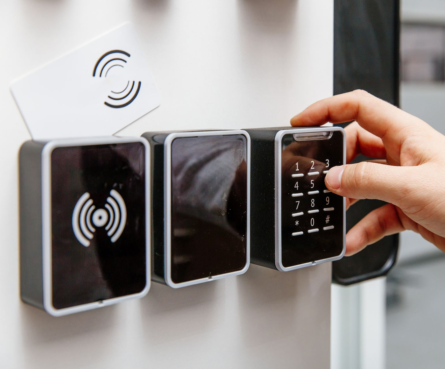 La main d'une personne saisissant un code PIN sur un clavier de système de sécurité à côté d'un lecteur de carte sur une surface blanche.