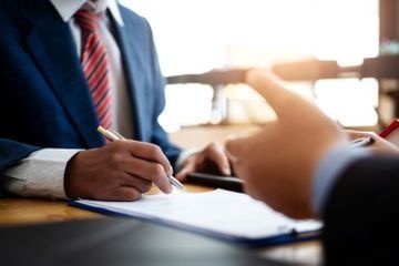 Empresario firmando un documento durante una reunión al otro lado de la mesa.