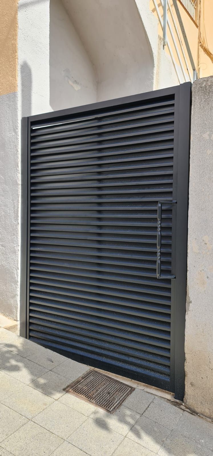 Una puerta de garaje negra está colocada al costado de un edificio.