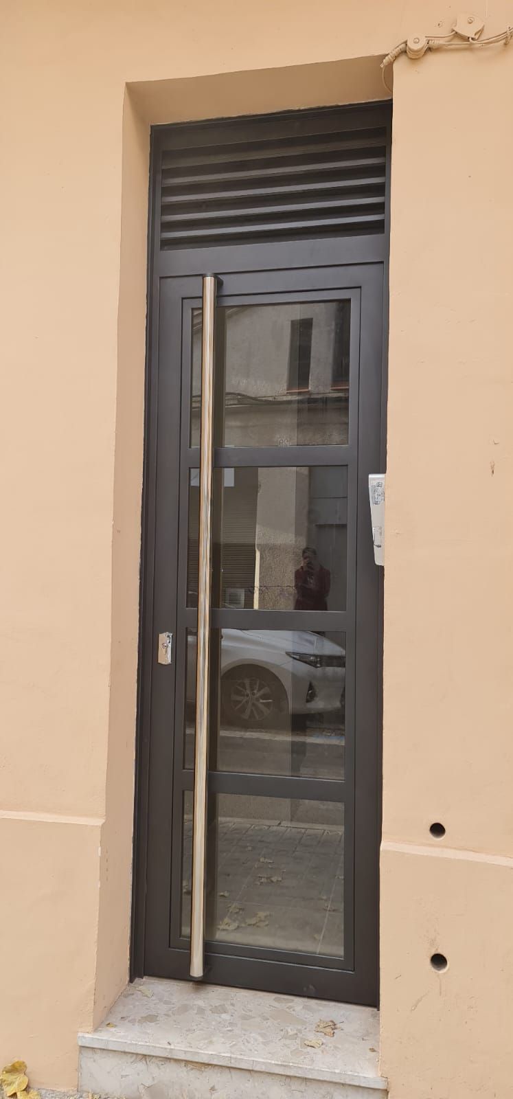 Una puerta negra con una puerta de vidrio está sentada al costado de un edificio.